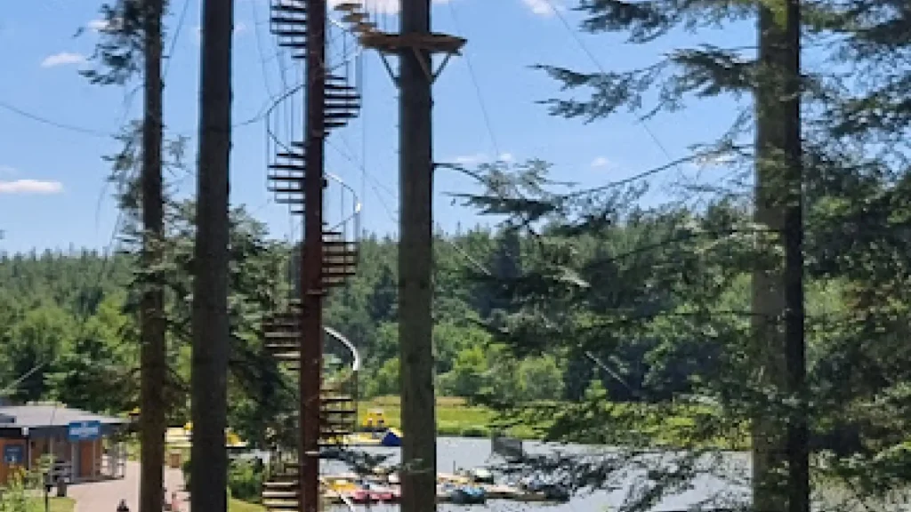 High ropes adventure course and spiral staircase among tall trees at Center Parcs Longleat, overlooking the forest and lake activities.