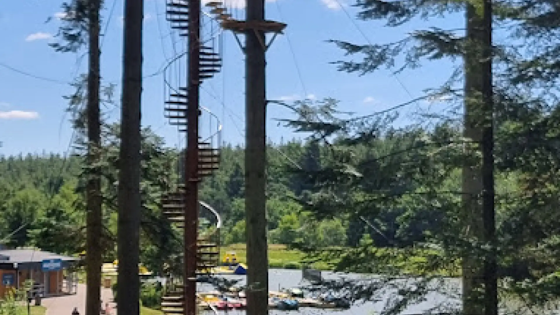 High ropes adventure course and spiral staircase among tall trees at Center Parcs Longleat, overlooking the forest and lake activities.