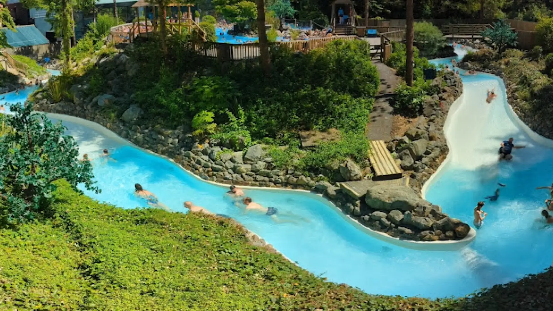Wild Water Rapids at Center Parcs Longleat with guests swimming through natural rock formations and lush greenery under sunny skies.