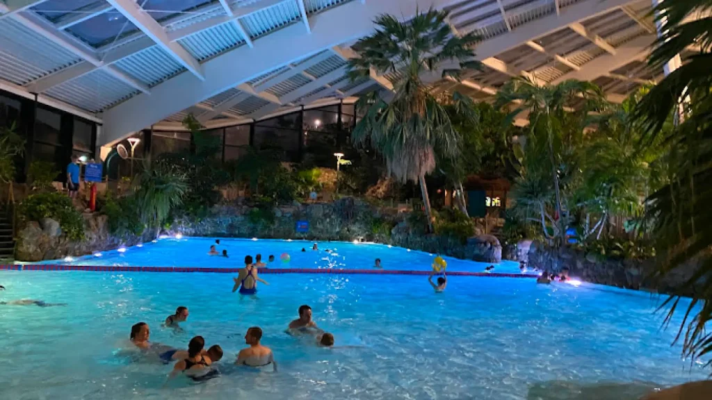 Guests swimming in the wave pool at Center Parcs Longleat’s Subtropical Swimming Paradise, lit by soft evening lights and tropical plants.