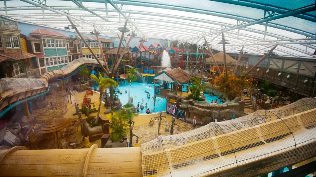 Busy indoor scene at Alton Towers Water Park with families enjoying pools, slides, and splash play areas beneath a tropical-style canopy.
