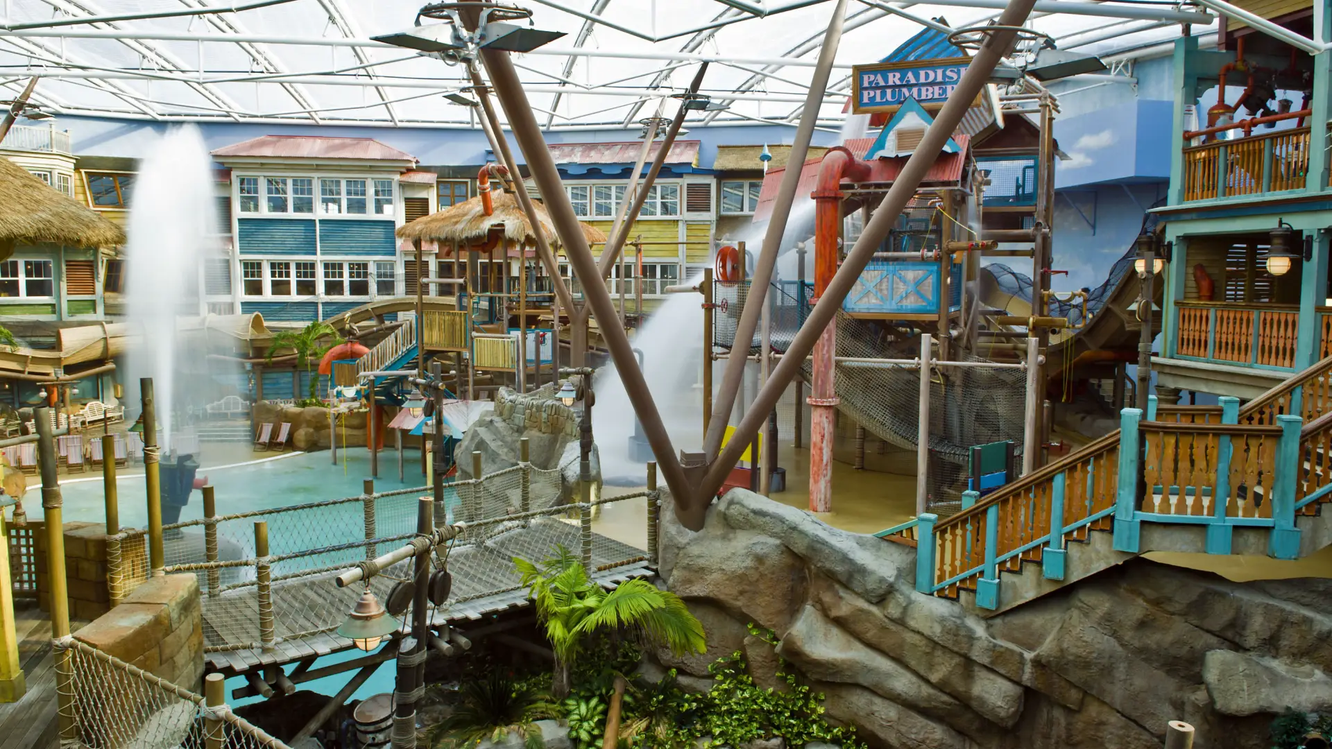 Water features and themed play structures at Alton Towers Water Park, including Paradise Plumbers, fountains, and wooden walkways in a tropical setting