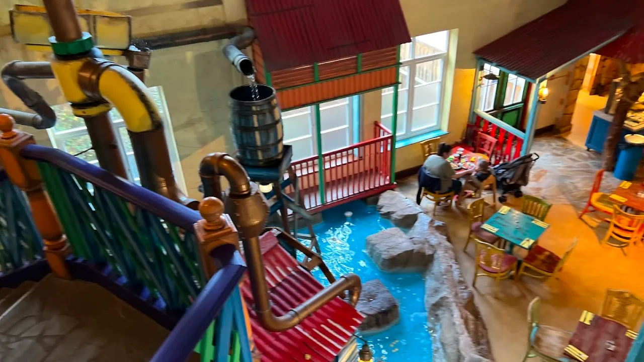 Themed restaurant inside Alton Towers Water Park in Staffordshire, showing colourful chairs, family dining tables, and a decorative water feature running between the seating areas, designed with a Caribbean tropical style.