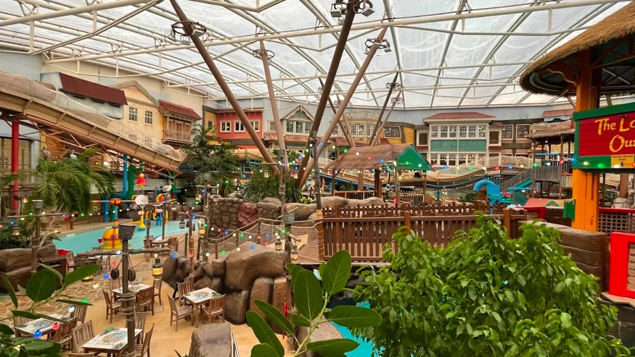 Indoor tropical-themed section of Alton Towers Water Park in Staffordshire, showing water slides, play areas, seating, and Caribbean-style décor beneath a large glass roof, with string lights adding to the vibrant atmosphere.