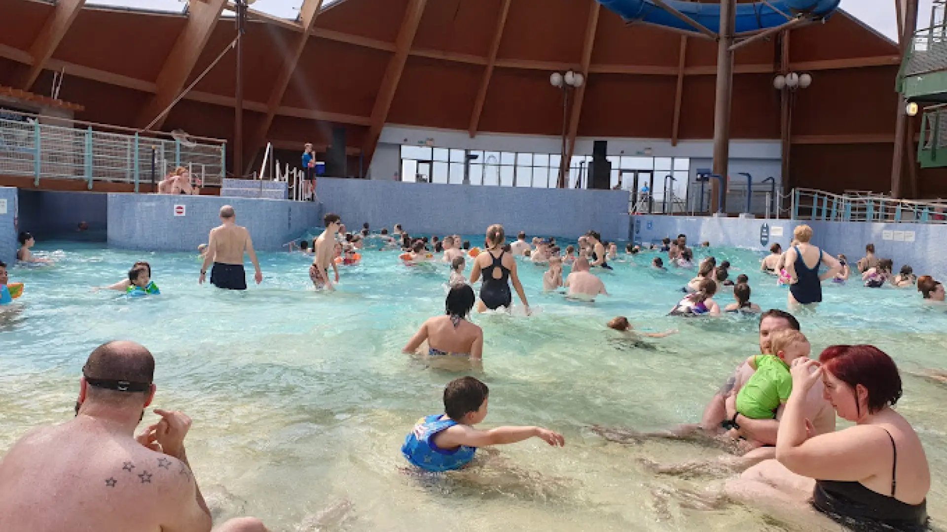 Crowded indoor wave pool with families, children, and toddlers enjoying the shallow water at Blue Lagoon Water Park, Bluestone Wales.
