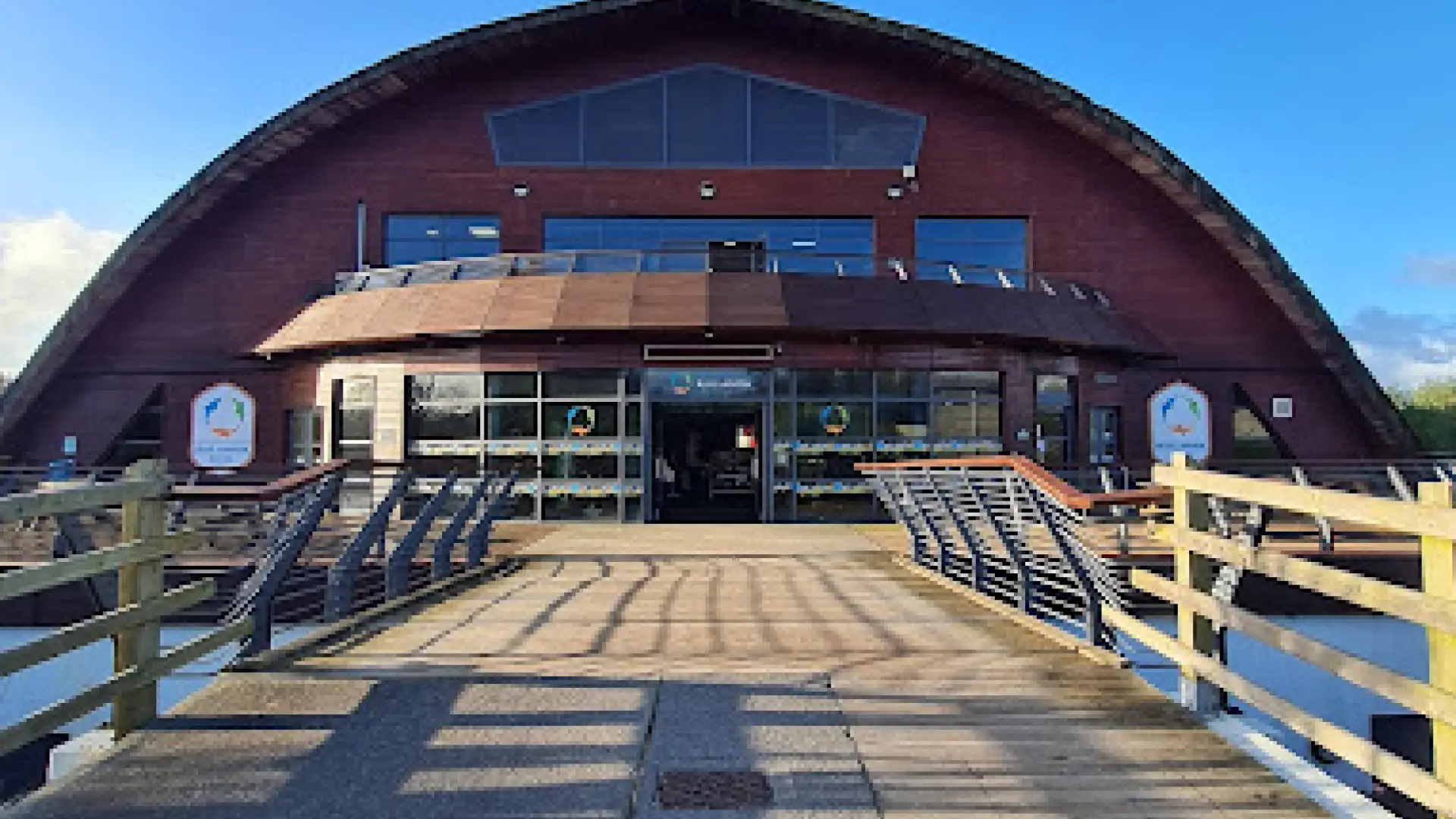 Exterior view of Blue Lagoon Water Park’s dome-shaped entrance with glass doors and wooden walkway at Bluestone National Park Resort in Pembrokeshire, Wales.