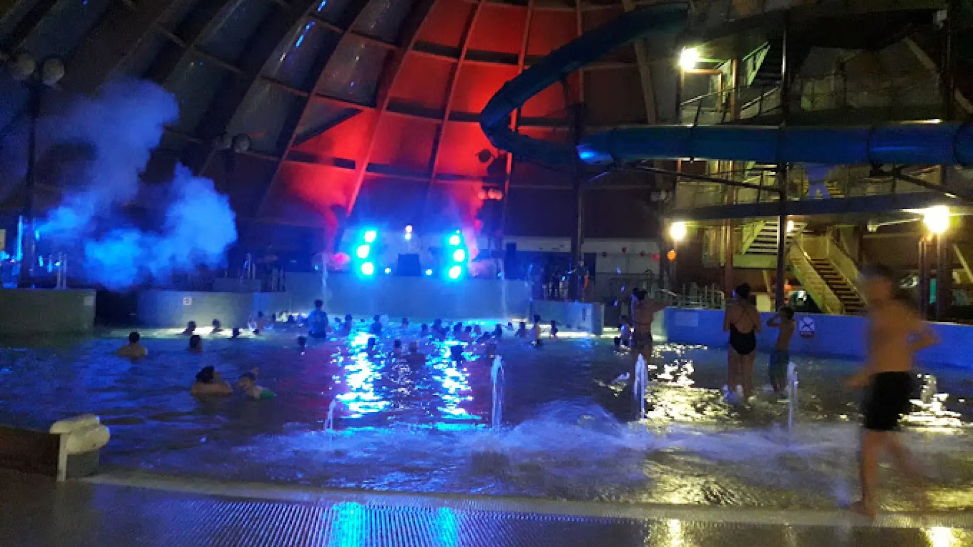Indoor night event at Blue Lagoon Water Park with colourful lighting, music setup, and guests enjoying a wave pool party under a glowing dome in Wales.