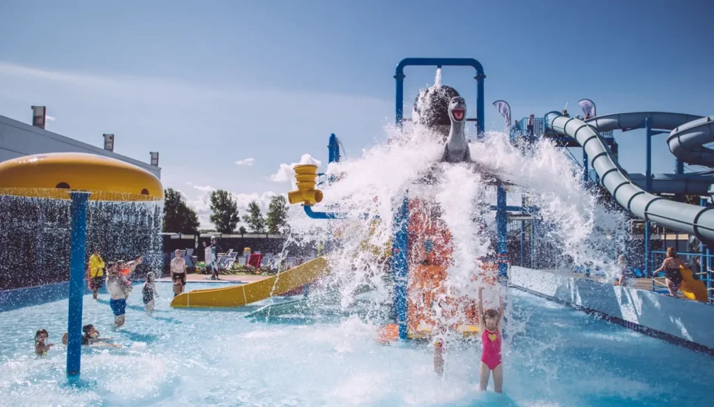 Children and families enjoy water play under a large tipping bucket feature at Brean Splash Waterpark, a popular water park with slides, splash zones, and fun attractions.