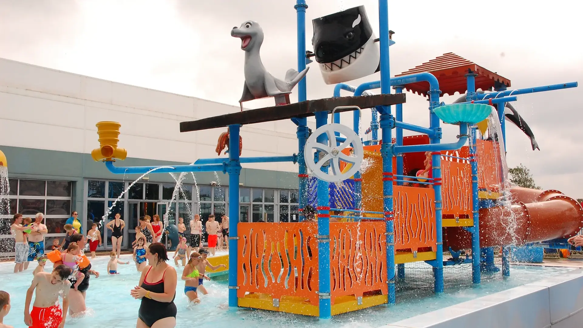Families playing at the colourful outdoor splash zone with water sprays and slides at Brean Splash Waterpark Somerset.