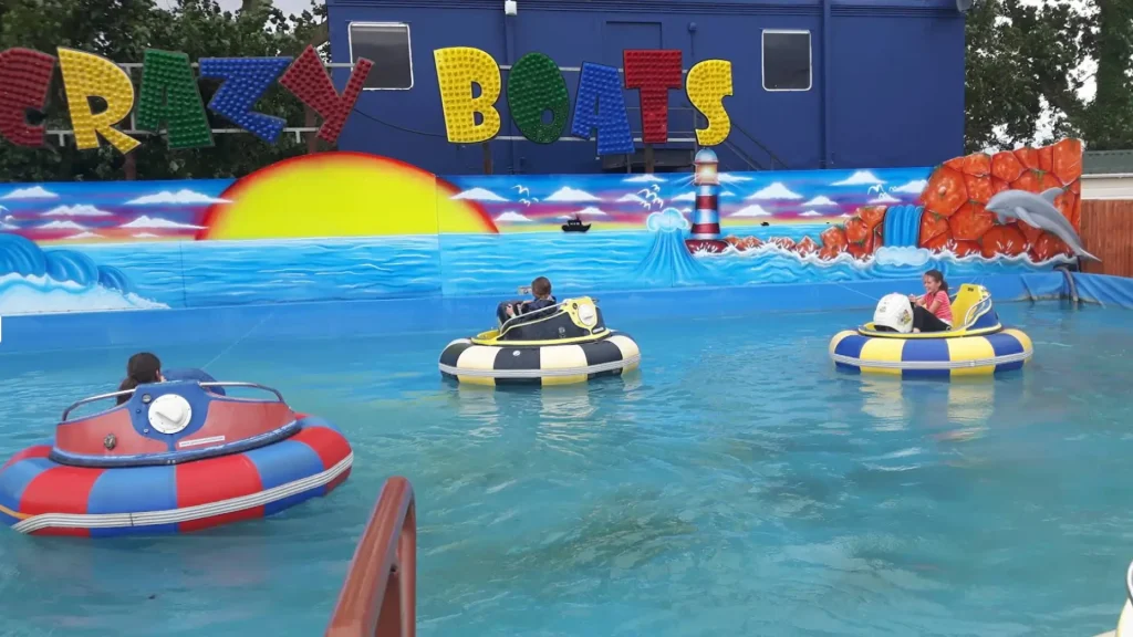 Children ride colorful bumper boats in the Crazy Boats attraction at Brean Splash Waterpark, a lively water park feature surrounded by vibrant murals and playful ocean-themed artwork.