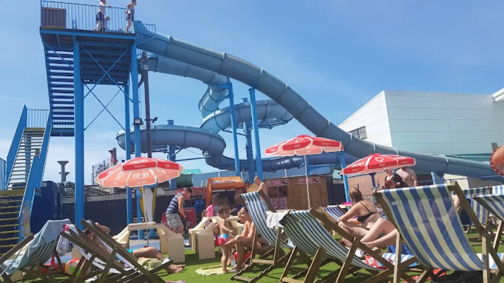 Guests relaxing on loungers and enjoying the large twisting outdoor water slides at Brean Splash Waterpark Somerset.