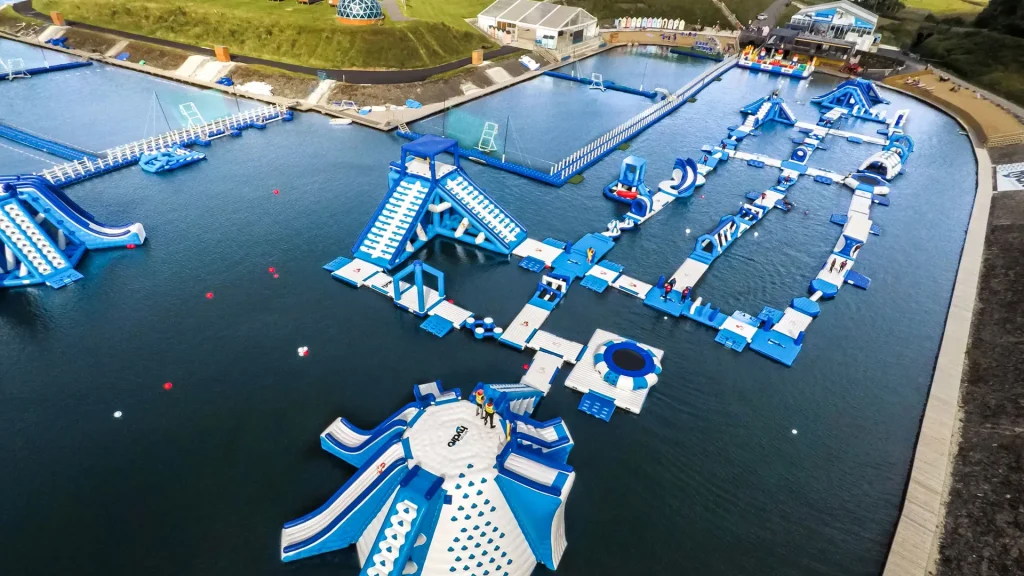Aerial view of Let's Go Hydro aqua park featuring giant inflatable water slides, obstacle courses, and splash zones on a lake in Northern Ireland.