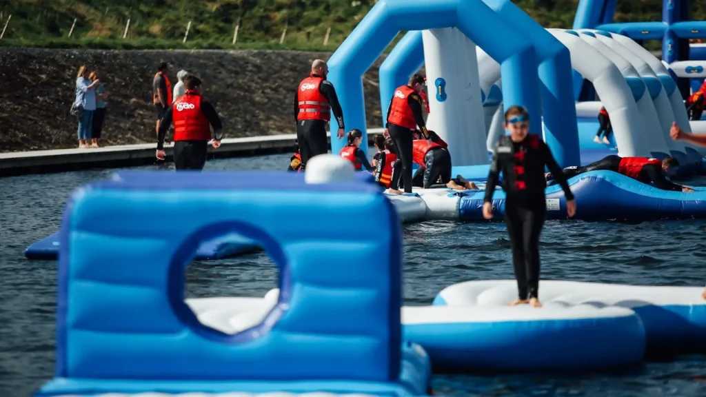 People wearing life jackets enjoying the inflatable obstacle course at Let's Go Hydro water park in Northern Ireland, with floating structures on the lake.
