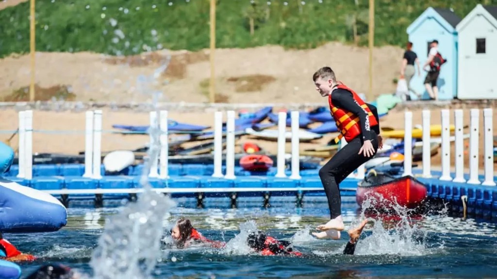 Boy in life jacket jumping into the water at Let's Go Hydro aqua park in Northern Ireland, with other guests swimming and splash zones in the background.