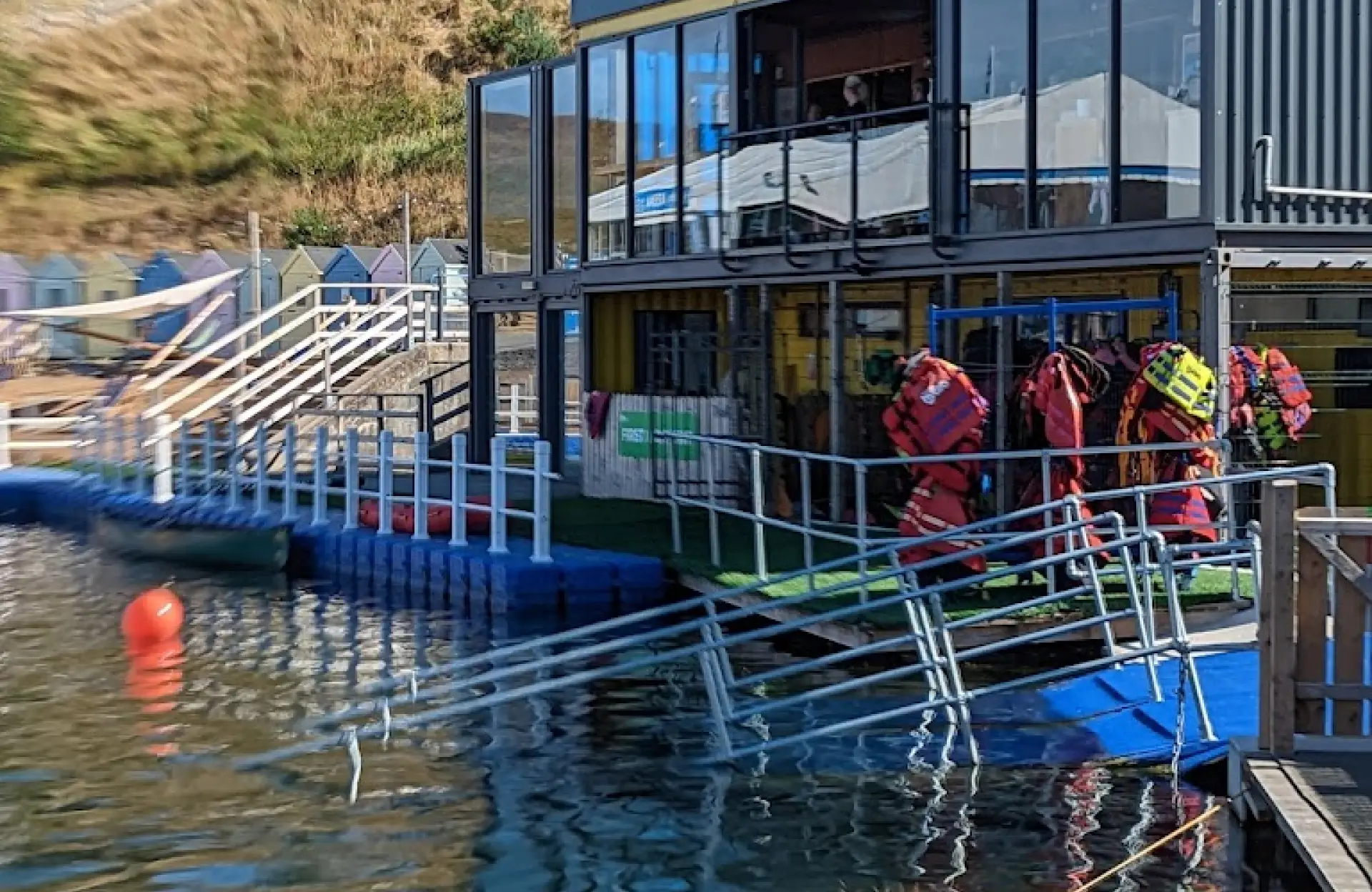 Life jackets hanging outside the Let's Go Hydro activity centre beside the lake, with colourful cabins and floating platforms nearby in Northern Ireland.