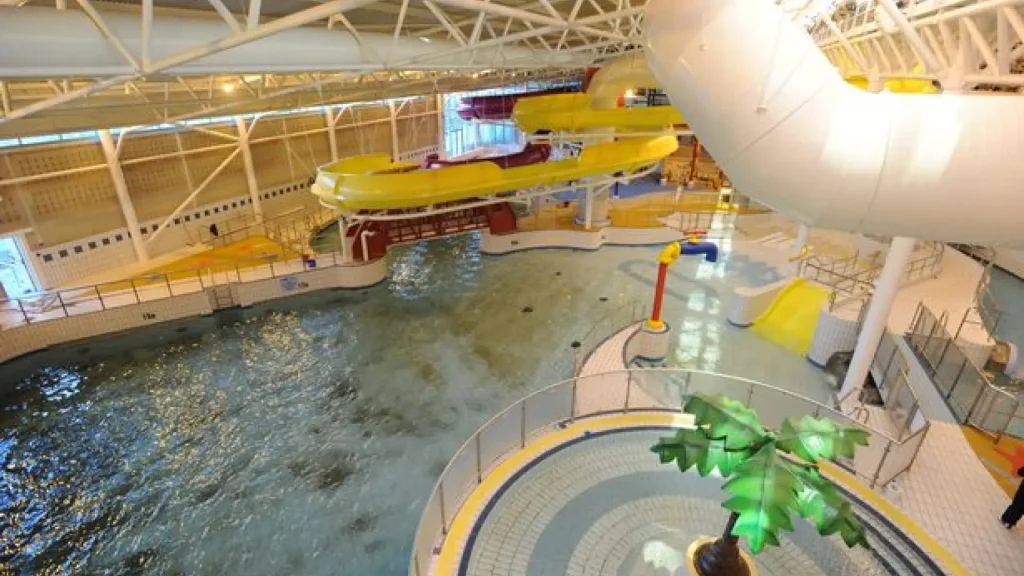 Interior of The Time Capsule Water Park Scotland showing wave pool, yellow flume slides and kids’ splash zone beneath white steel roof.