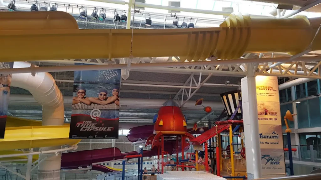 Inside The Time Capsule Water Park Scotland: yellow Storm Chasers slide crosses ceiling above red rocket and Tsunami wave pool banners.