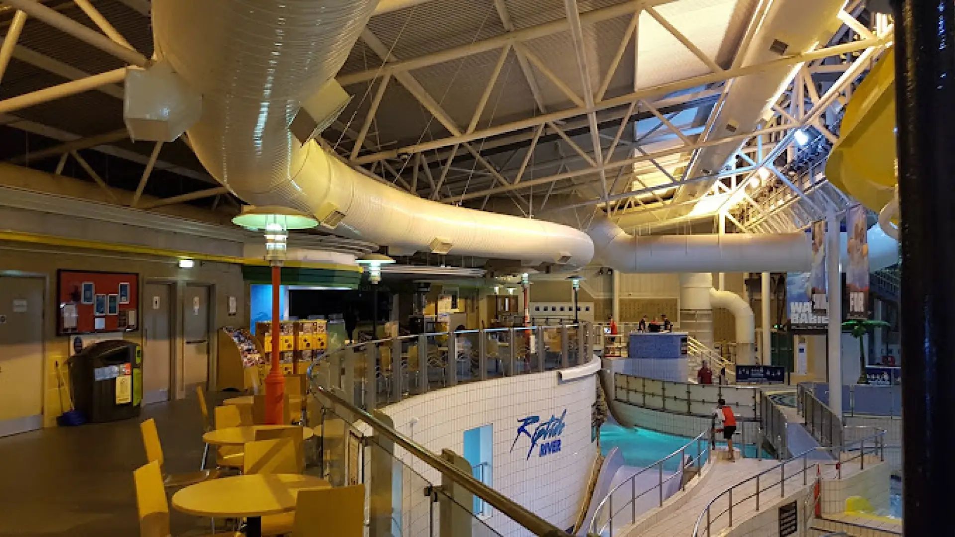 Upper deck café seating overlooks Riptide River at The Time Capsule Water Park Scotland, giant white slide overhead.