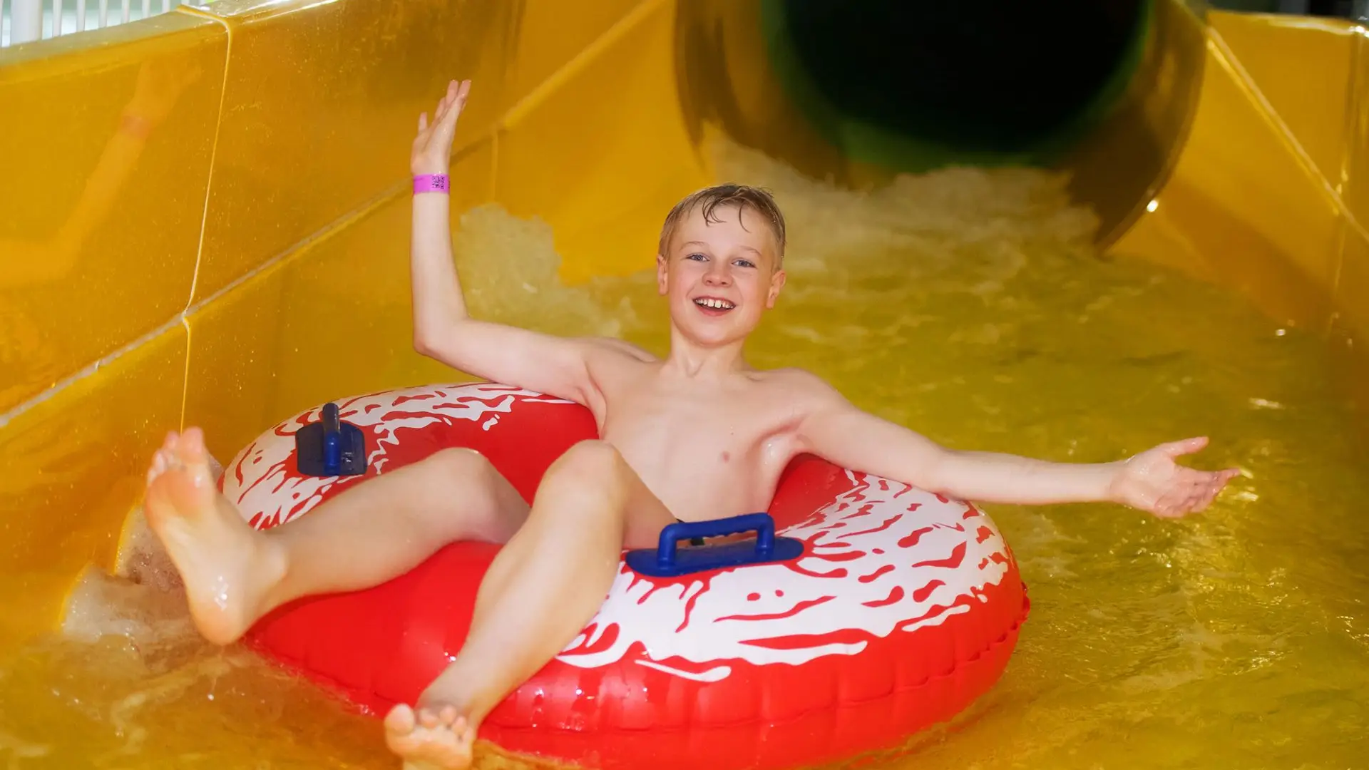 Boy riding a red inflatable ring on a yellow water slide at The Wave Waterpark, New Union Street, Coventry.