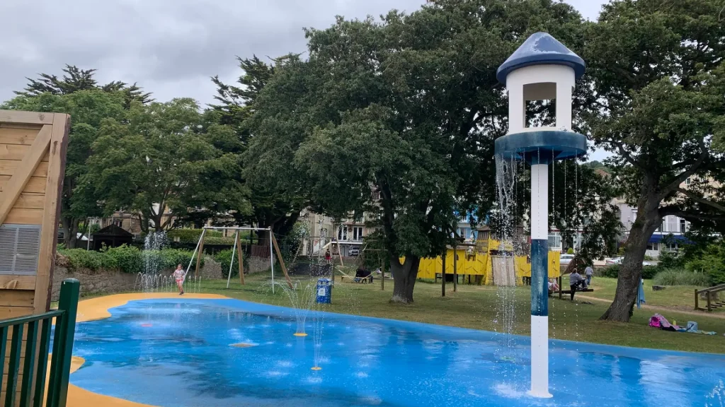 Children playing in the splash zone at Water Adventure Play Park in Weston-super-Mare with tall water feature and swings in the background.