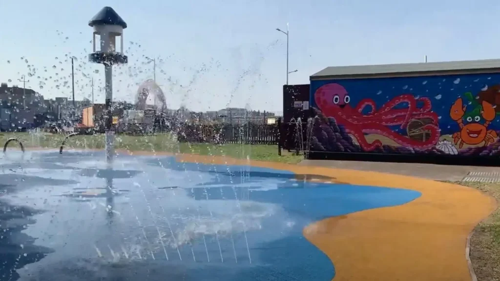 Splash pad at Water Adventure Play Park in Weston-super-Mare with water jets spraying and colourful sea life mural in the background.