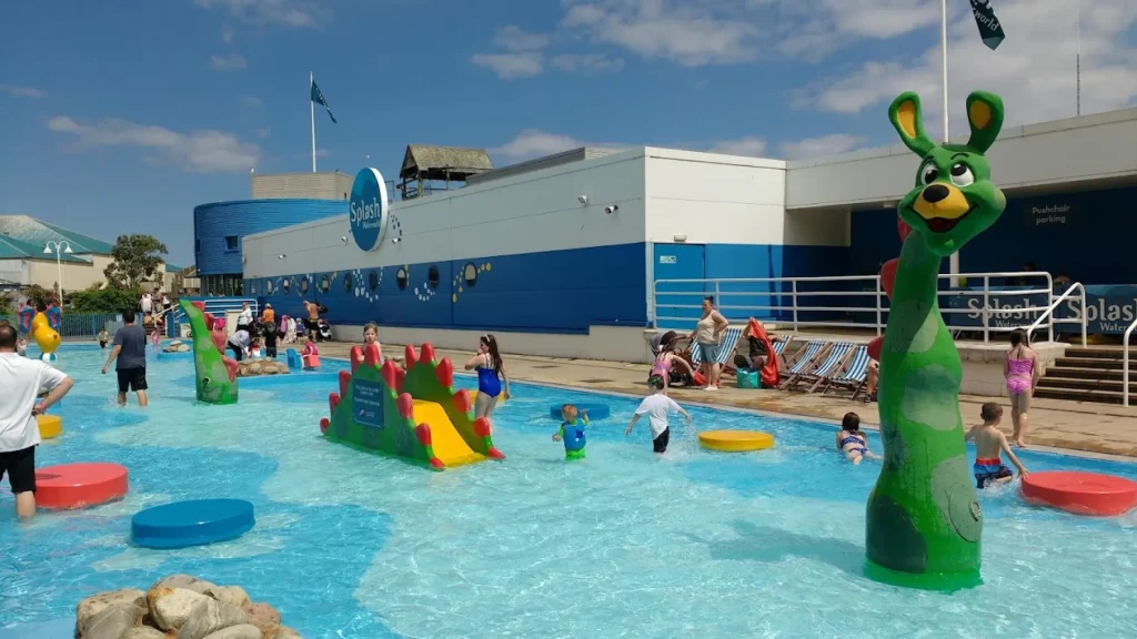 Children and families playing in the outdoor pool area at Butlins Splash Waterworld Minehead water park, featuring slides, splash features, and colourful characters.