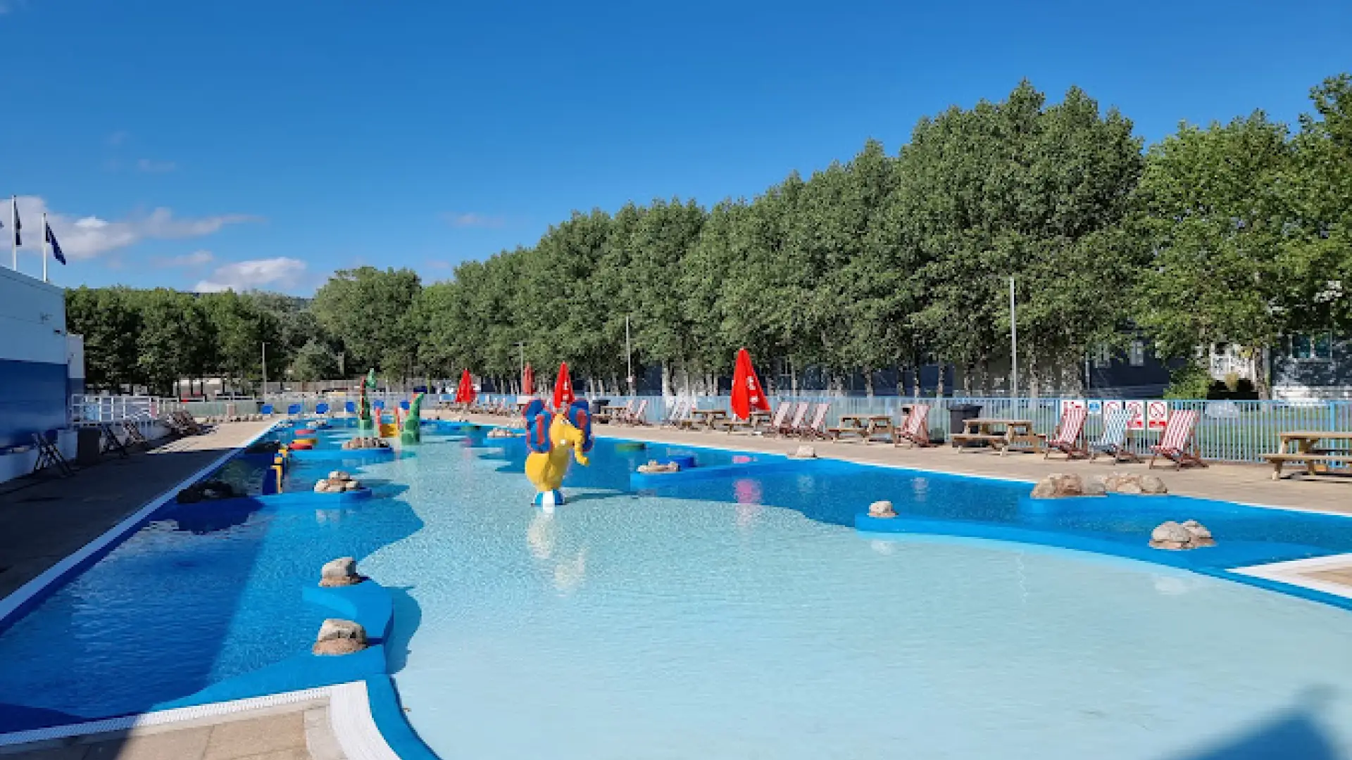Shallow outdoor pool with colorful water features and sun loungers at Butlins Splash Waterworld Minehead on a sunny day.