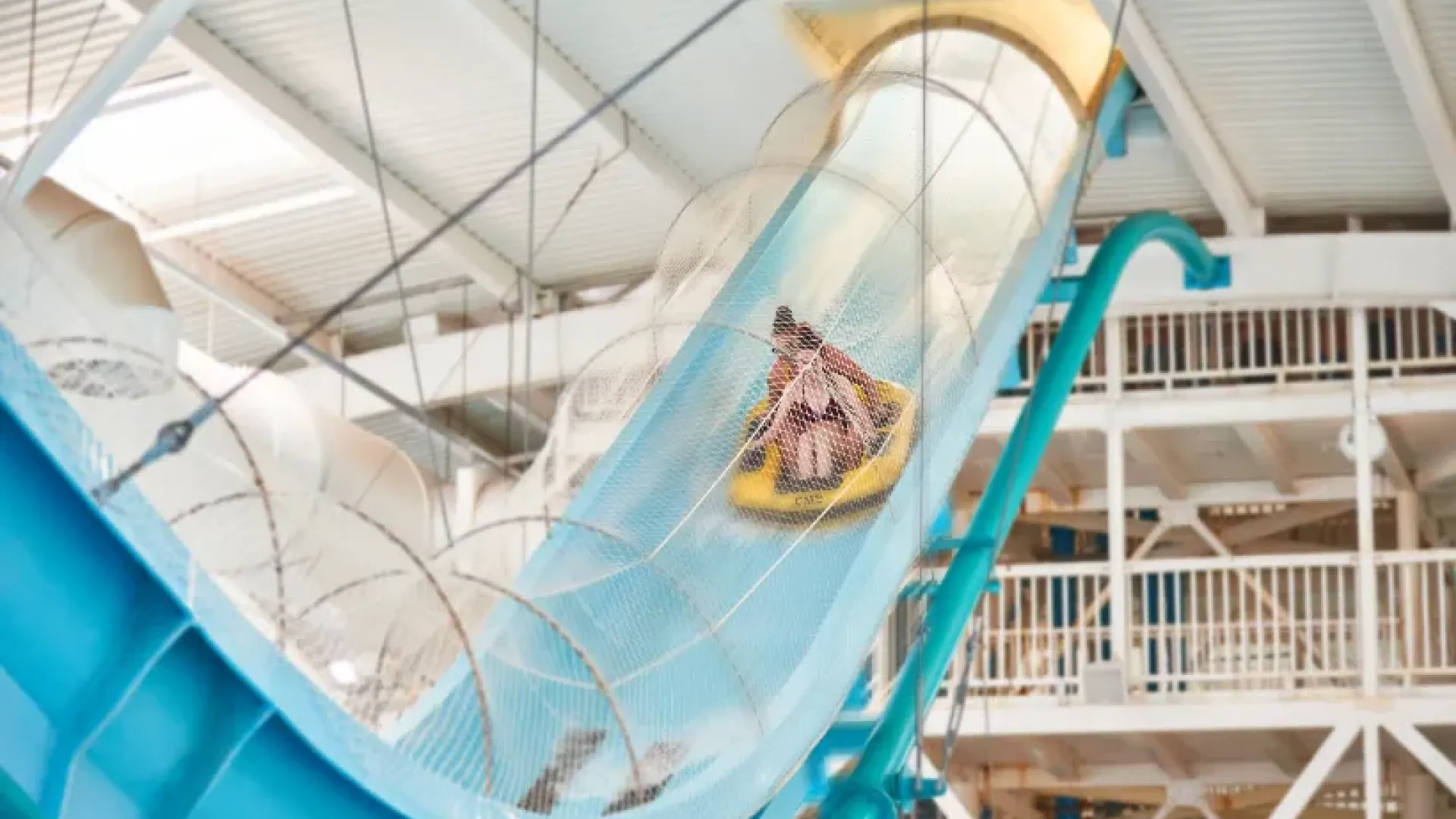 Guests riding a yellow inflatable down the Master Blaster slide inside Butlins Splash Waterworld Minehead water park, surrounded by safety nets and indoor structures.