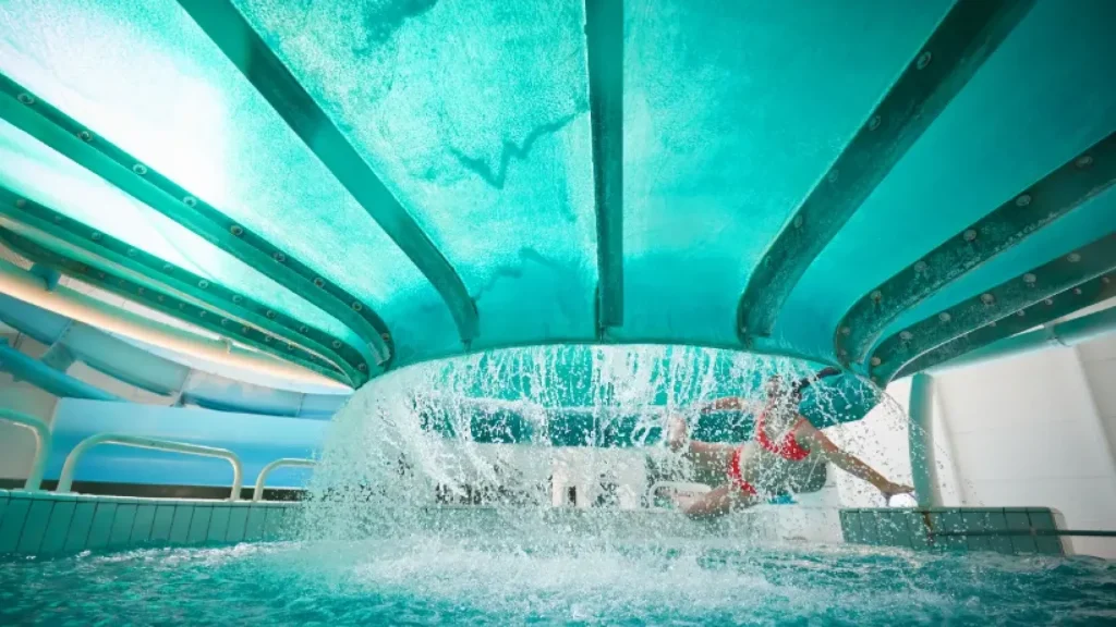 Person splashing into the pool after exiting the Space Bowl ride at Butlins Splash Waterworld Minehead water park, with water cascading all around.