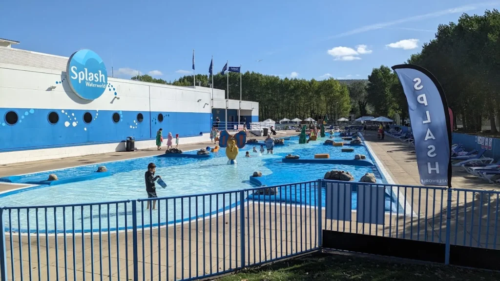 Children and families playing in the outdoor pool at Butlins Splash Waterworld Minehead water park, with interactive water features and loungers nearby.