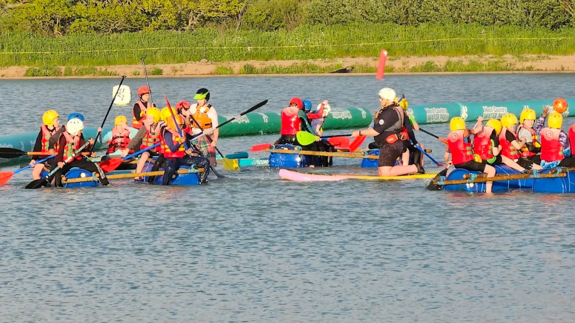 Children and instructors paddling on homemade rafts during a group activity session at West Country Water Park, wearing life jackets and helmets.