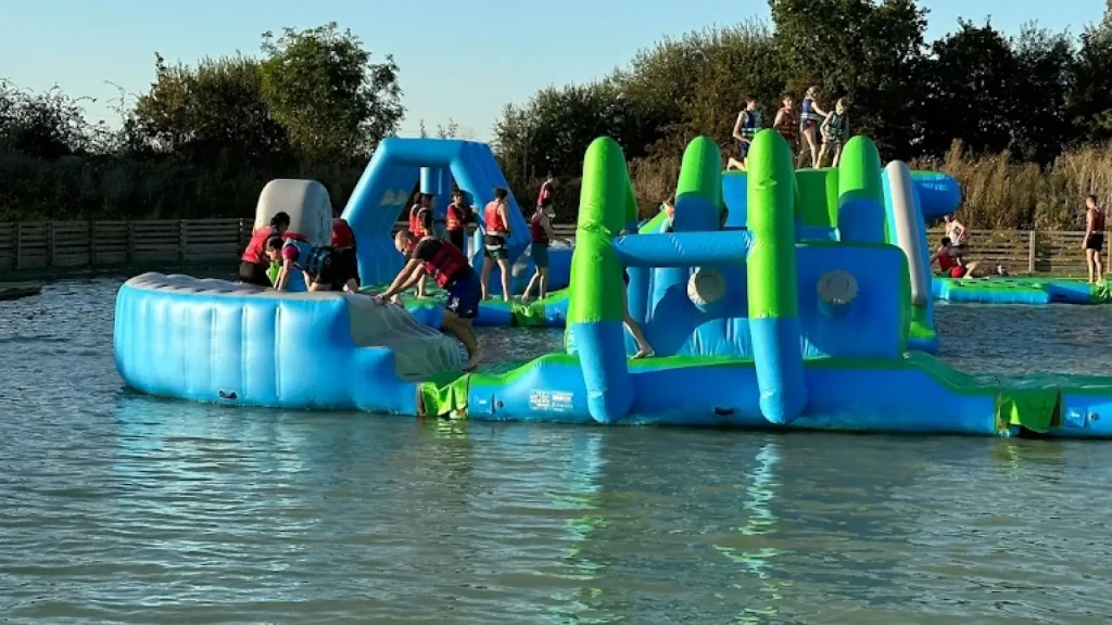 Visitors climbing and navigating inflatable obstacles at the aqua park course at West Country Water Park, enjoying sunny weather and outdoor fun.
