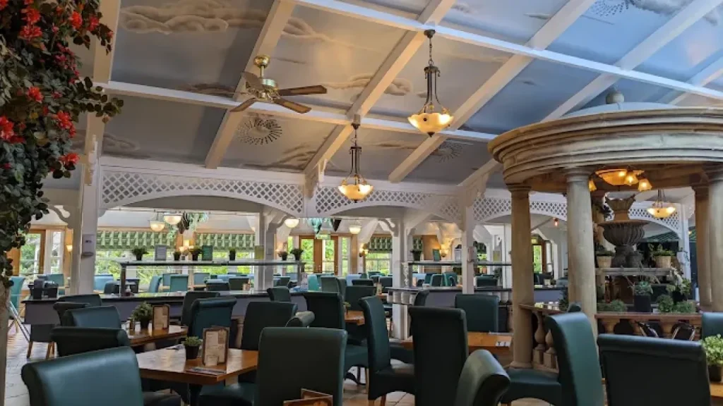 Spacious restaurant with decorative ceiling, greenery, and fountain feature at Alton Towers Hotel dining area