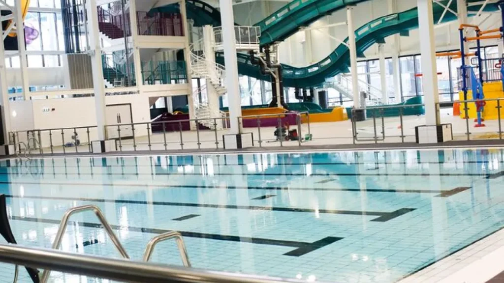 Interior of Andersonstown Leisure Centre showing clean swimming lanes, twisting indoor water slides, and colourful kids’ play structures.