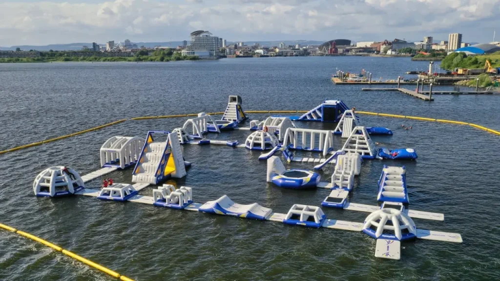 Aerial view of Aqua Park Cardiff inflatable obstacle course on a lake with city skyline.