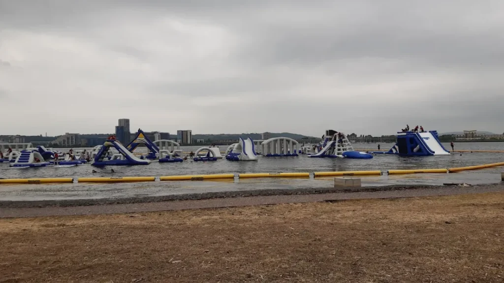 Wide lakefront view of Aqua Park Cardiff inflatable water park on a cloudy day.