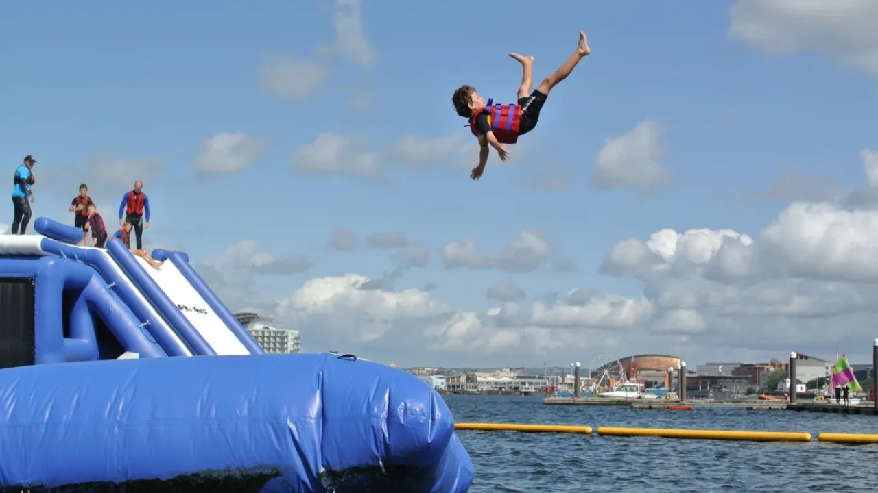 Person flying mid-air from inflatable jump at Aqua Park Cardiff water park.