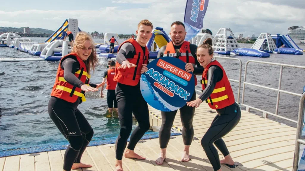 Smiling group in wetsuits posing in front of Aqua Park Cardiff inflatables.