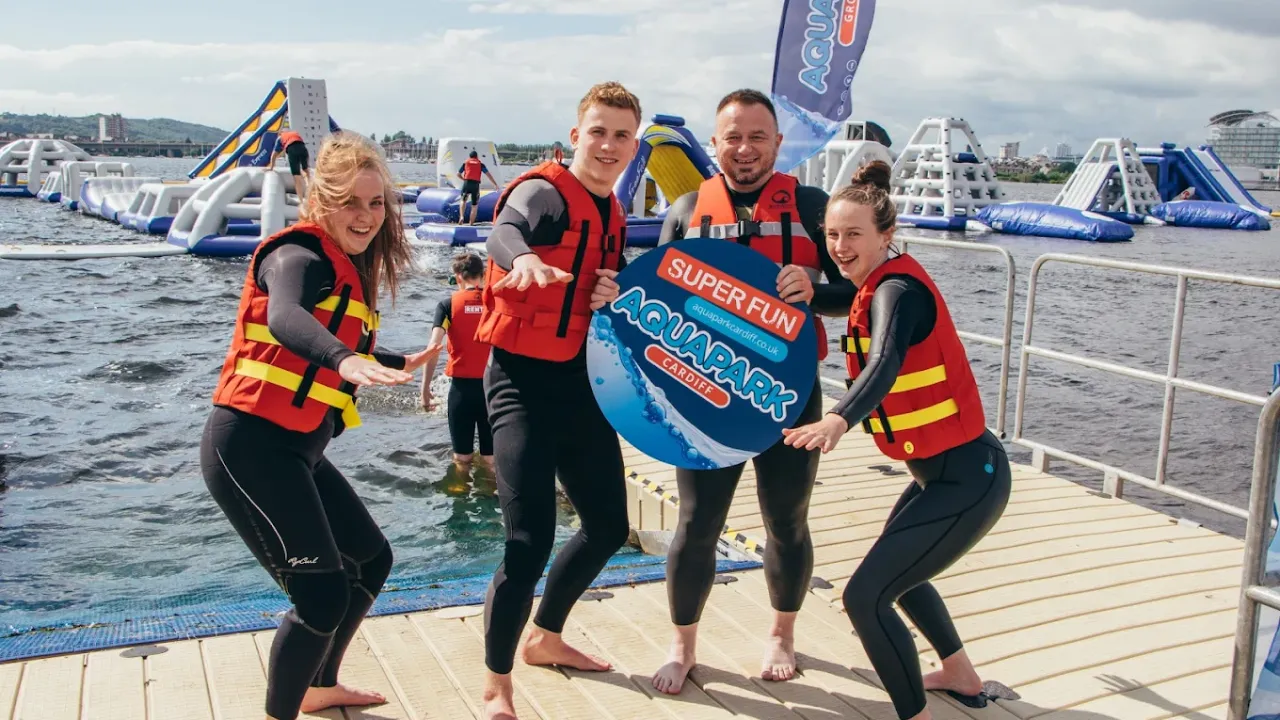 Smiling group in wetsuits posing in front of Aqua Park Cardiff inflatables.
