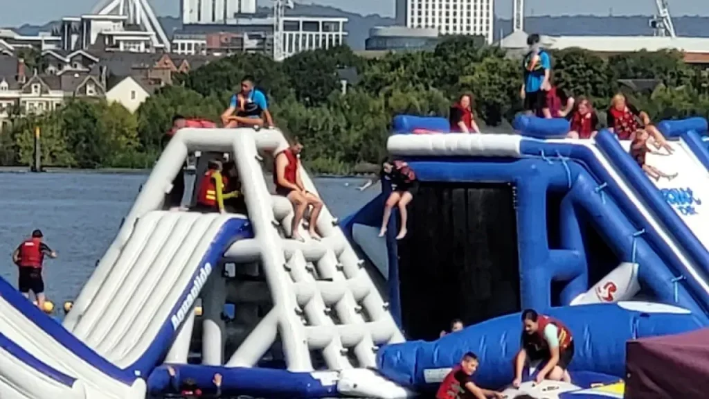 Crowds enjoying tall inflatable water slides and climbing frames at Aqua Park Cardiff.