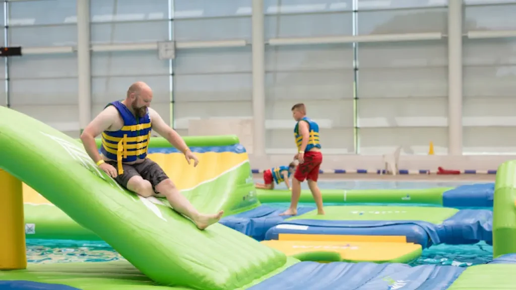 Adult and child navigating the Aqua Challenge inflatable obstacle course at Bangor Aurora Leisure Centre indoor pool.