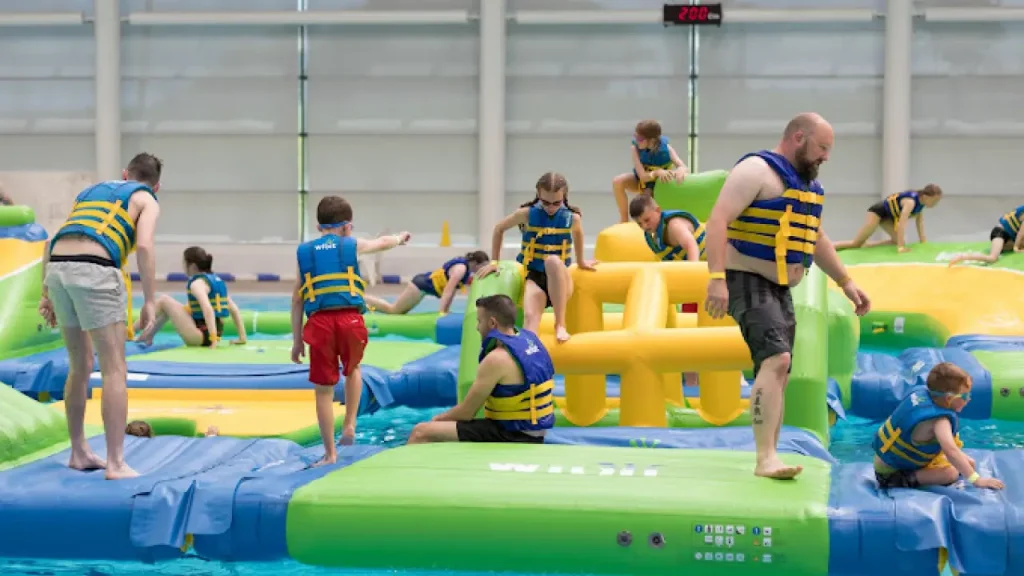 Children and adults enjoying the Aqua Challenge inflatable obstacle course at Bangor Aurora Leisure Centre indoor pool.