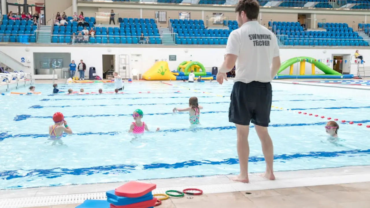Swimming teacher supervising a children’s swim class at Bangor Aurora Leisure Centre with poolside spectator seating.