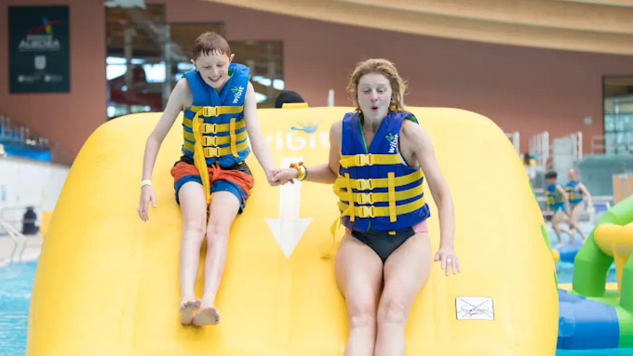 Child and adult sliding down the Aqua Challenge inflatable slide at Bangor Aurora Leisure Centre, wearing life jackets.