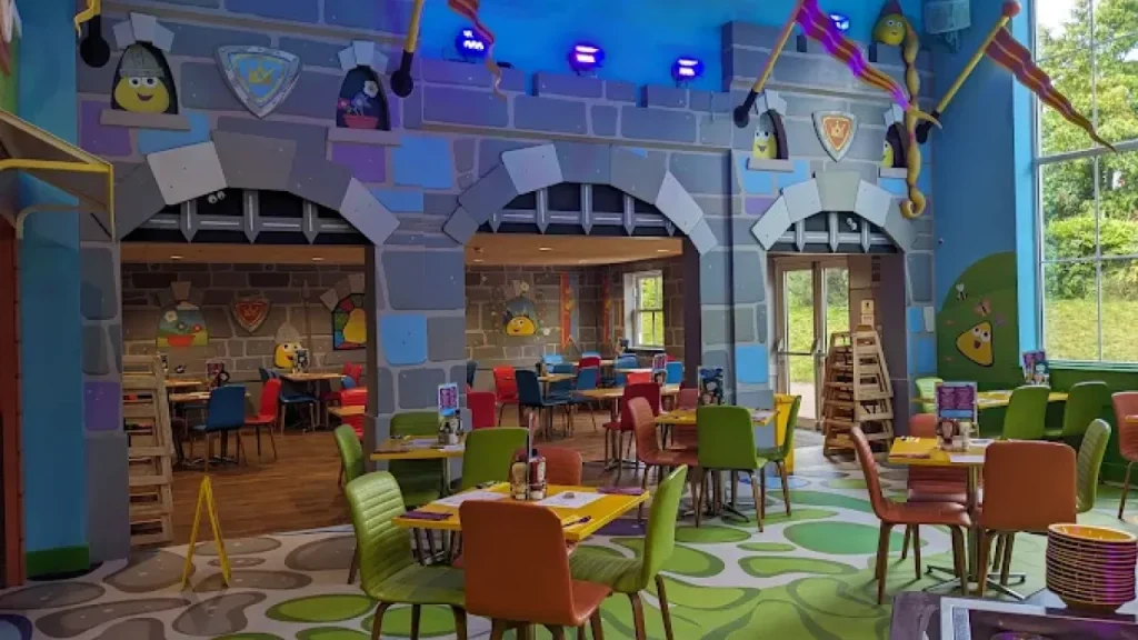 Bright castle-themed restaurant at CBeebies Land Hotel with colourful chairs, cartoon wall art, and family dining tables