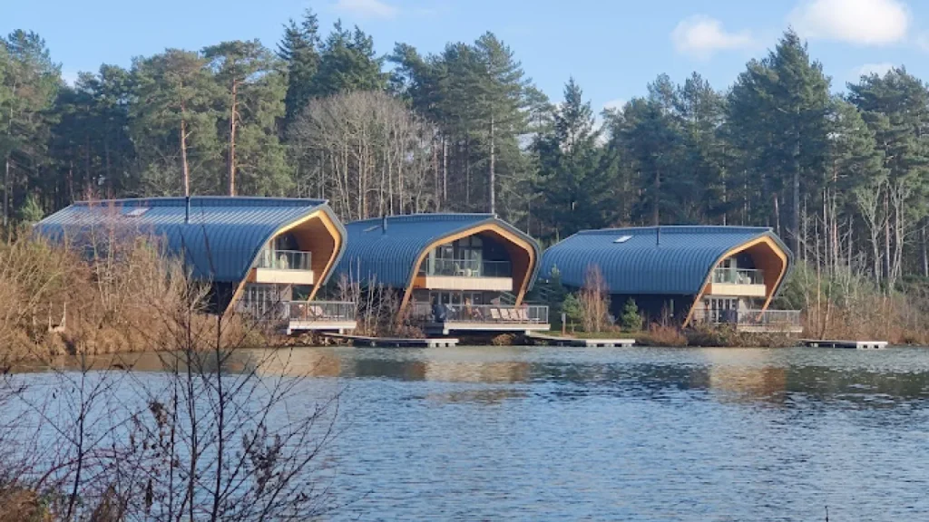 Modern curved-roof lodges on the water’s edge at Center Parcs Elveden Forest, surrounded by woodland and offering private lakefront views.
