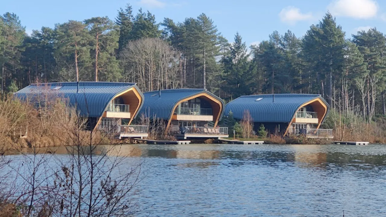Modern curved-roof lodges on the water’s edge at Center Parcs Elveden Forest, surrounded by woodland and offering private lakefront views.