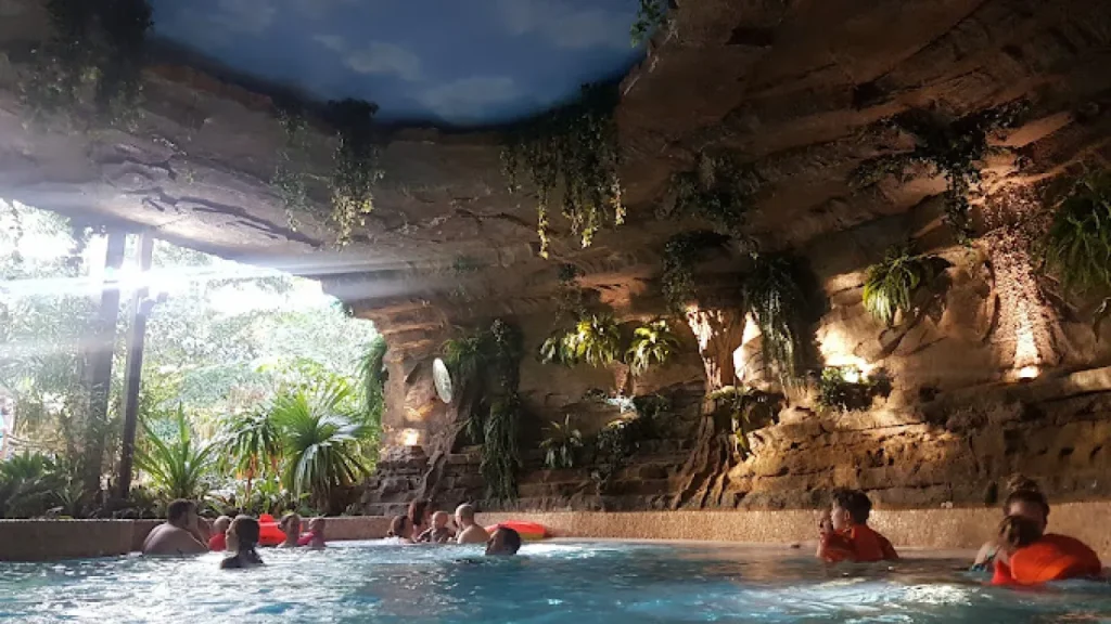 Guests relaxing in the tropical-themed grotto pool at Center Parcs Elveden Forest, surrounded by rock walls, greenery, and natural light.