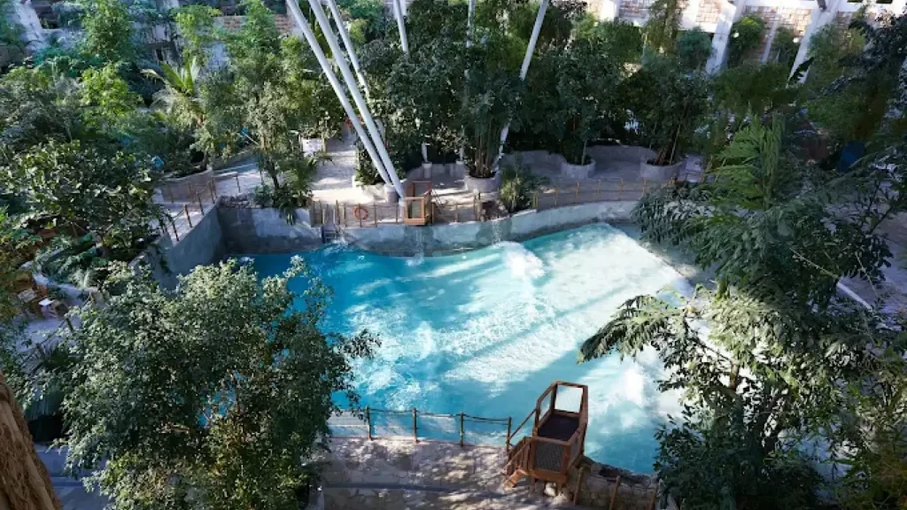 Indoor wave pool at Center Parcs Woburn Forest, encircled by tropical plants and trees, with clear blue water and splash zones.