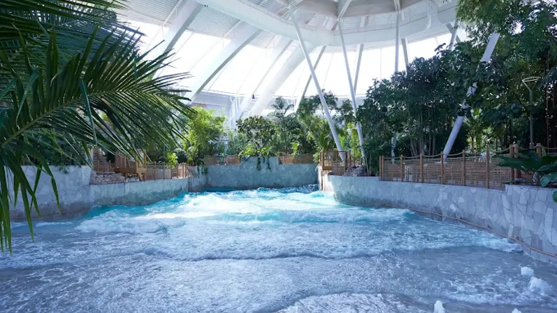 Wave pool at Center Parcs Woburn Forest with gentle waves, tropical greenery, and a bright, airy dome ceiling.